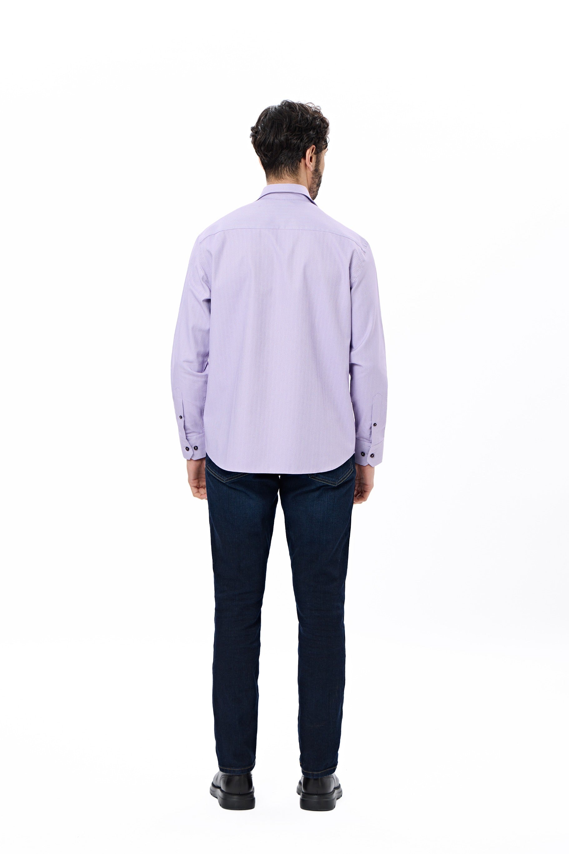 Man wearing a light purple shirt and dark jeans on a white background